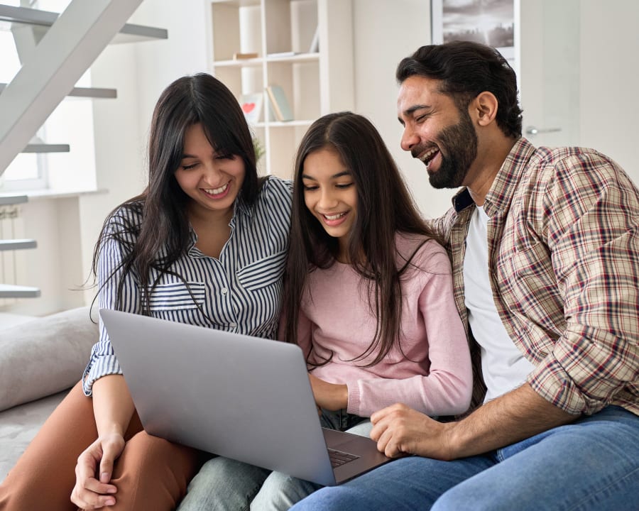 Une jeune famille composée d'une femme, d'un homme et d'un jeune adolescent est assise ensemble sur un canapé en regardant un ordinateur portable.