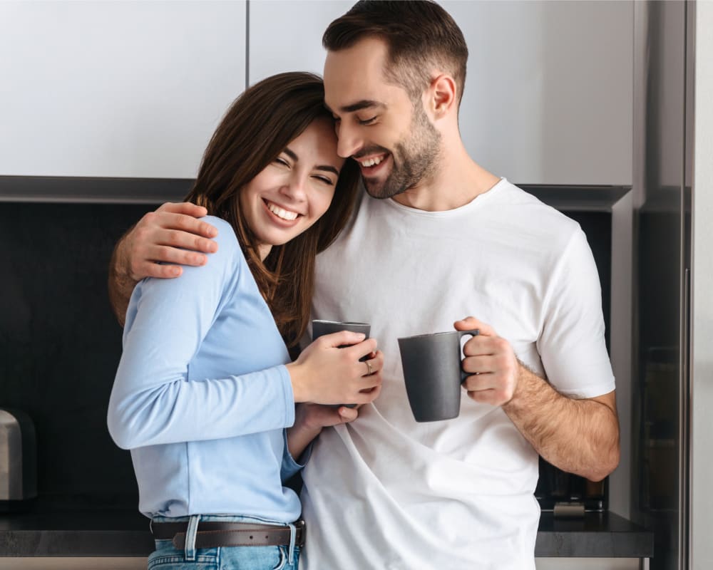 Un jeune couple s'enlace tout en tenant des tasses.