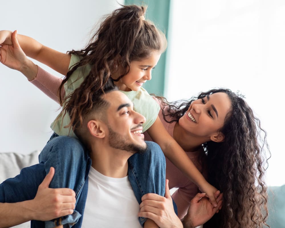 Une jeune fille est assise sur les épaules de son père tout en souriant à sa mère.